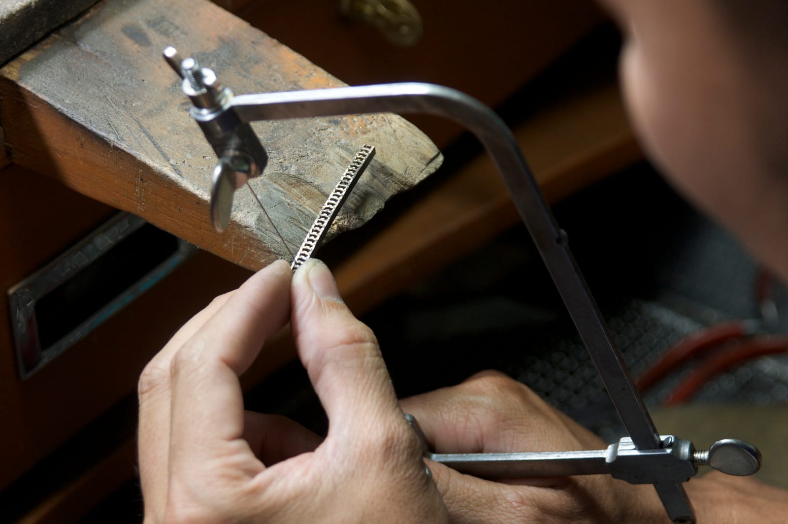 A jeweller's saw pierces a set strip against the bench pin.