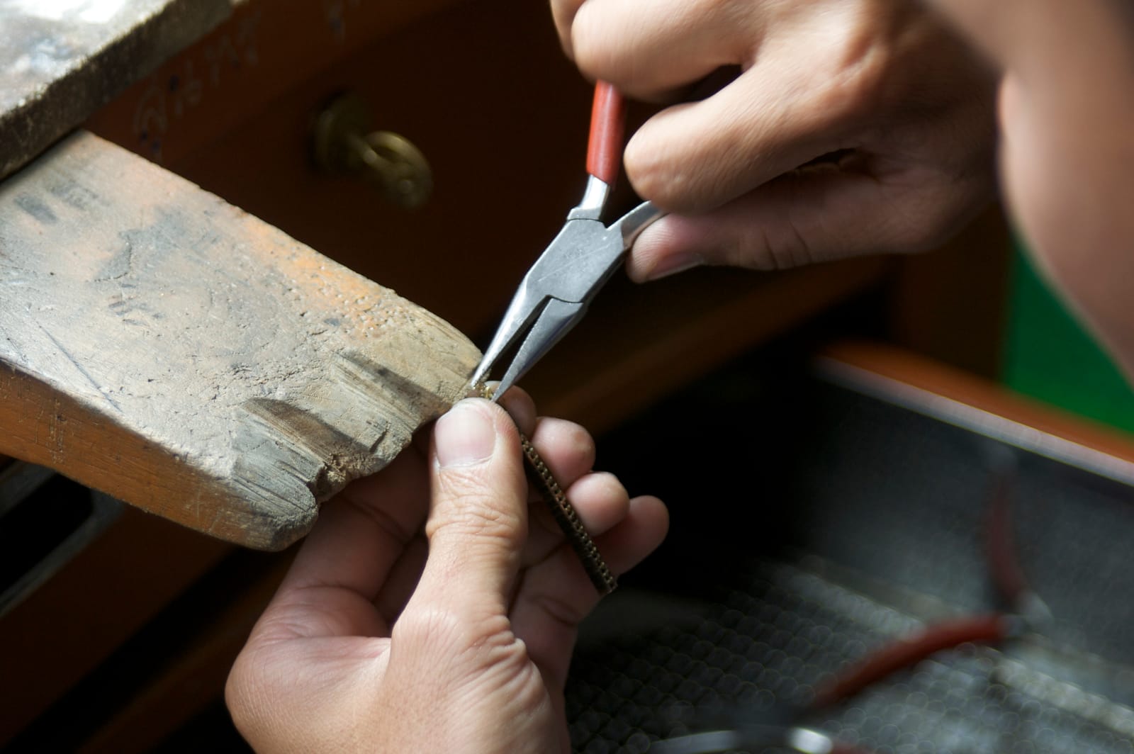 Chain-nose pliers close a set strip against the bench pin.